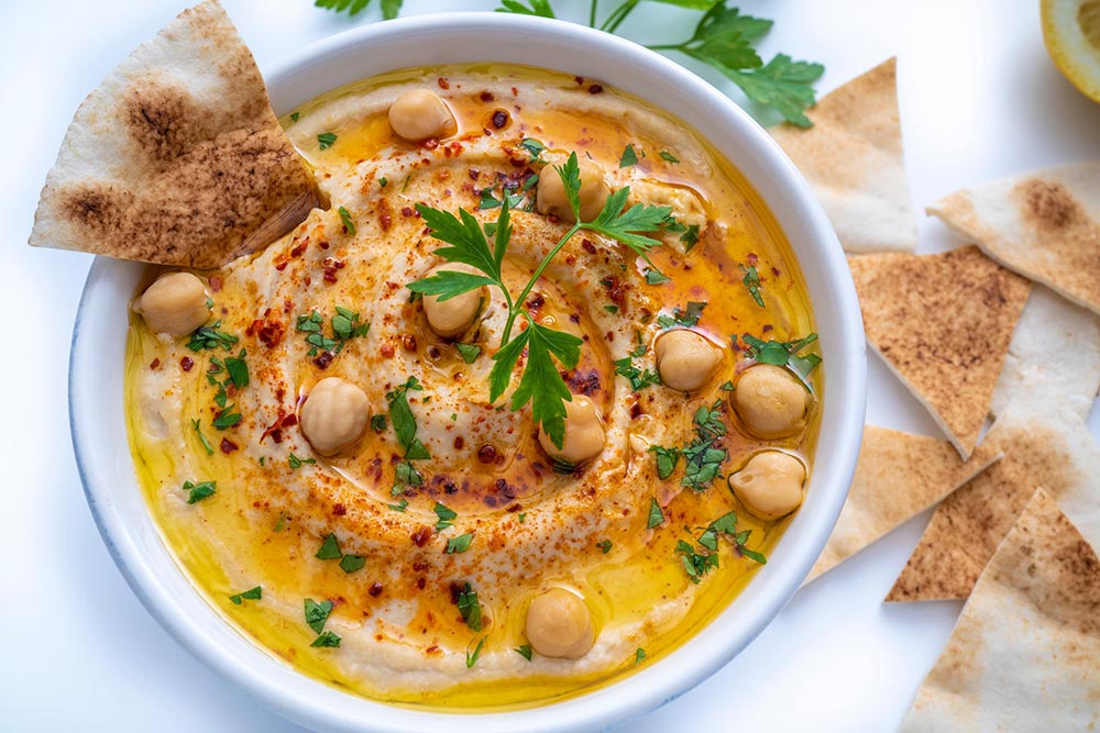An overhead view of creamy hummus topped with full chickpeas and pita wedges for dipping. 