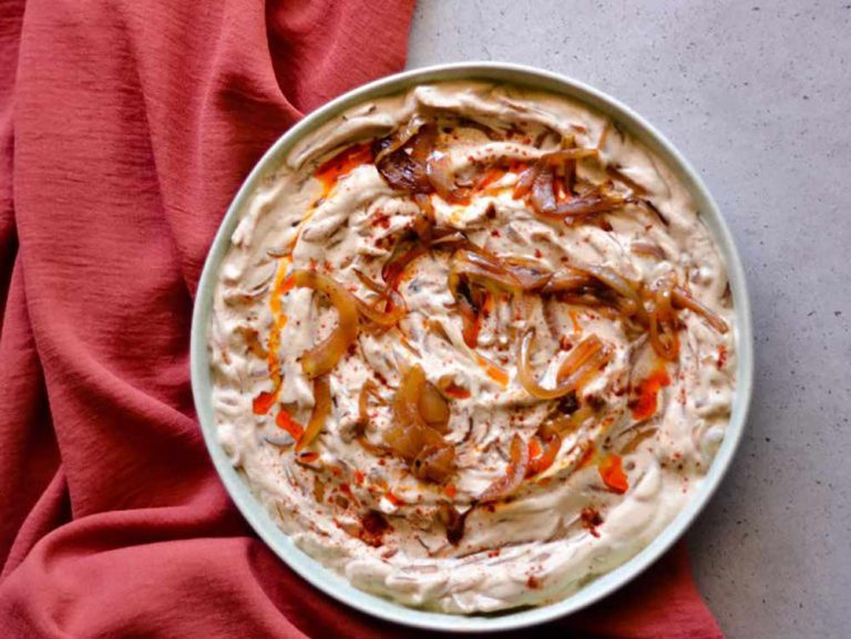 A bowl of creamy, dairy-free onion dip topped with caramelised onions and paprika oil, served as a plant-based starter.