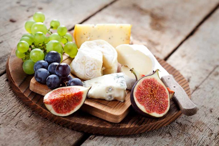 A wooden board featuring a variety of plant-based cheeses, green and black grapes, and sliced figs.