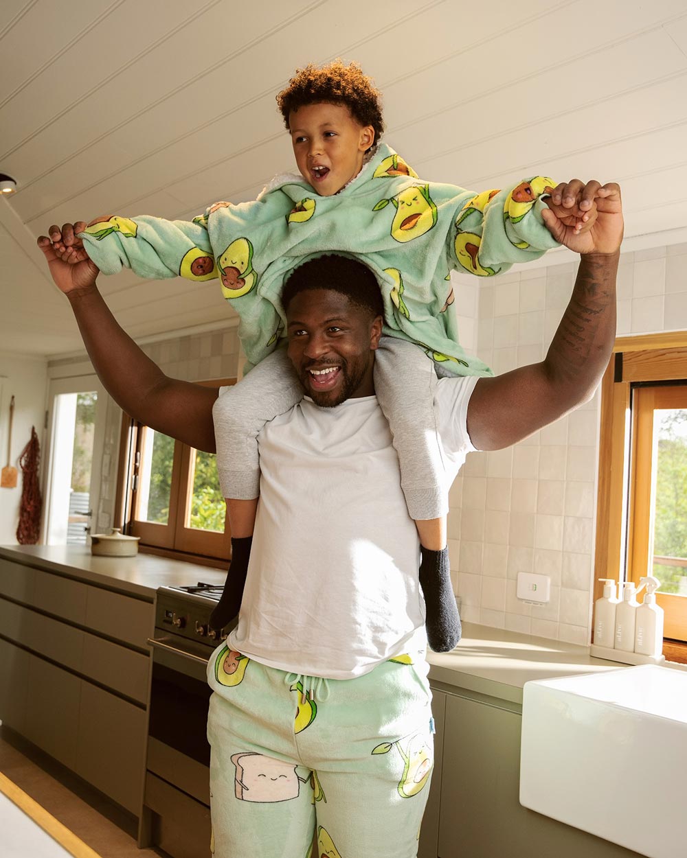 A father holds his son on his shoulders, while they're both wearing their avocado design oodies. 