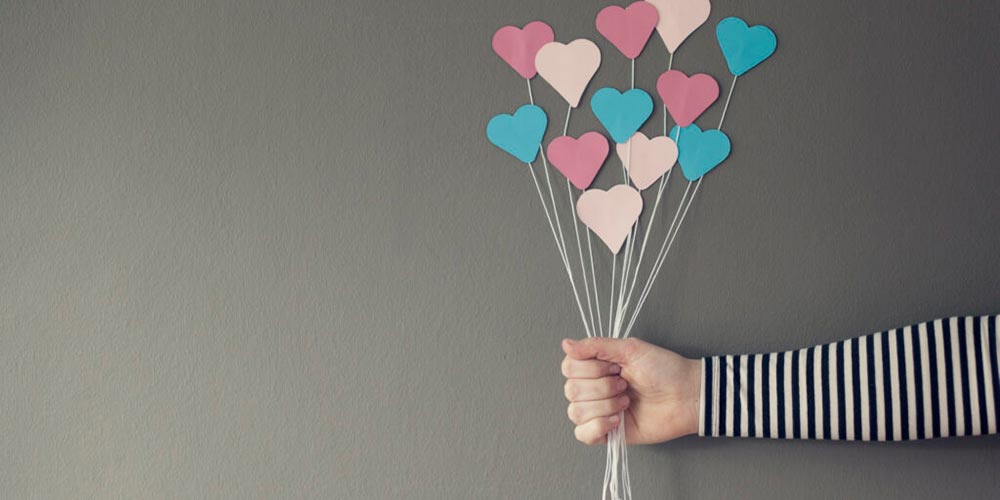 A hand holds out a bunch of coloured hearts on a stick, giving a balloon effect.