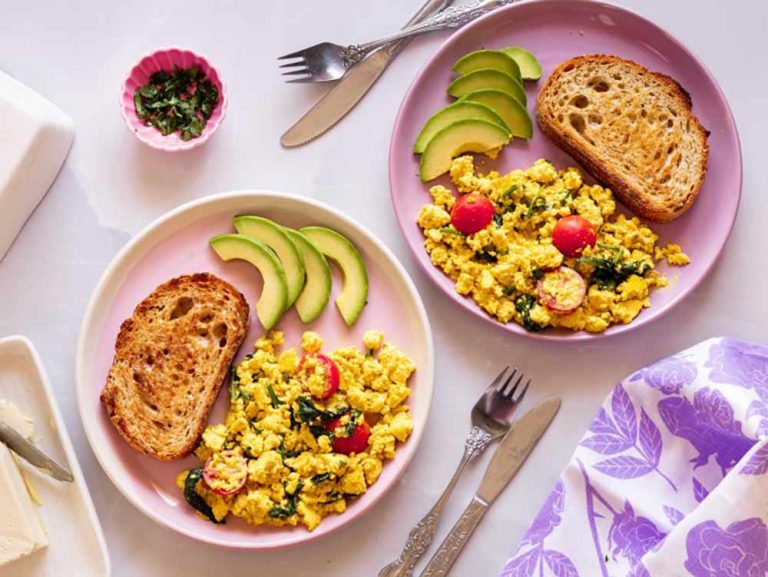 Two plates of scrambled tofu with spinach and cherry tomatoes, served with avocado slices and sourdough as part of our favourite plant-based tofu dishes.