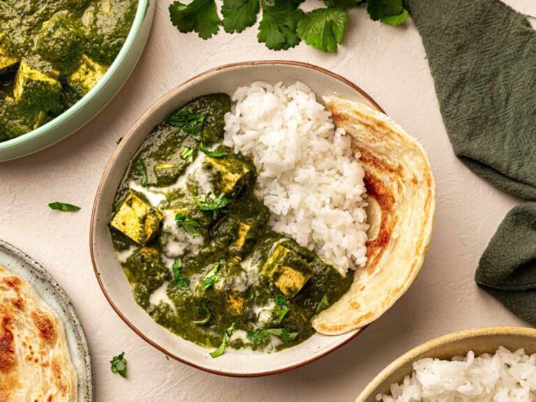 A bowl of palak tofu, a staple of plant-based meals, served with white rice and a piece of flatbread.