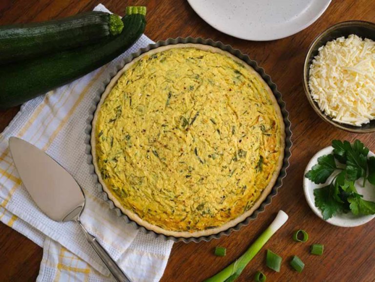 Courgette and plant-based cheese quiche in a tart tin, served with grated vegan cheese, parsley, and shallots, perfect for vegetarian meals.