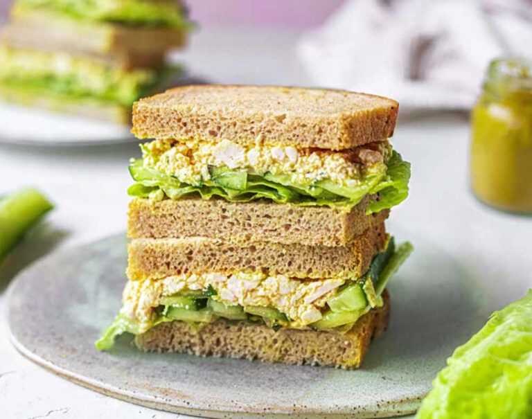 A double-decker sandwich on wholemeal bread filled with a plant-based tofu egg salad, lettuce, and cucumber on a plate.