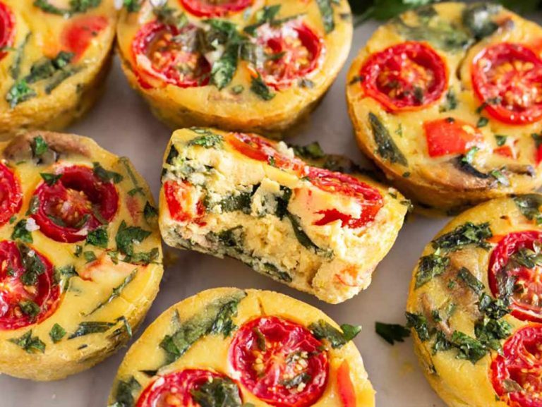 Plant-based mini frittatas topped with cherry tomatoes and herbs, with one cut in half to show the texture in this tofu dish.