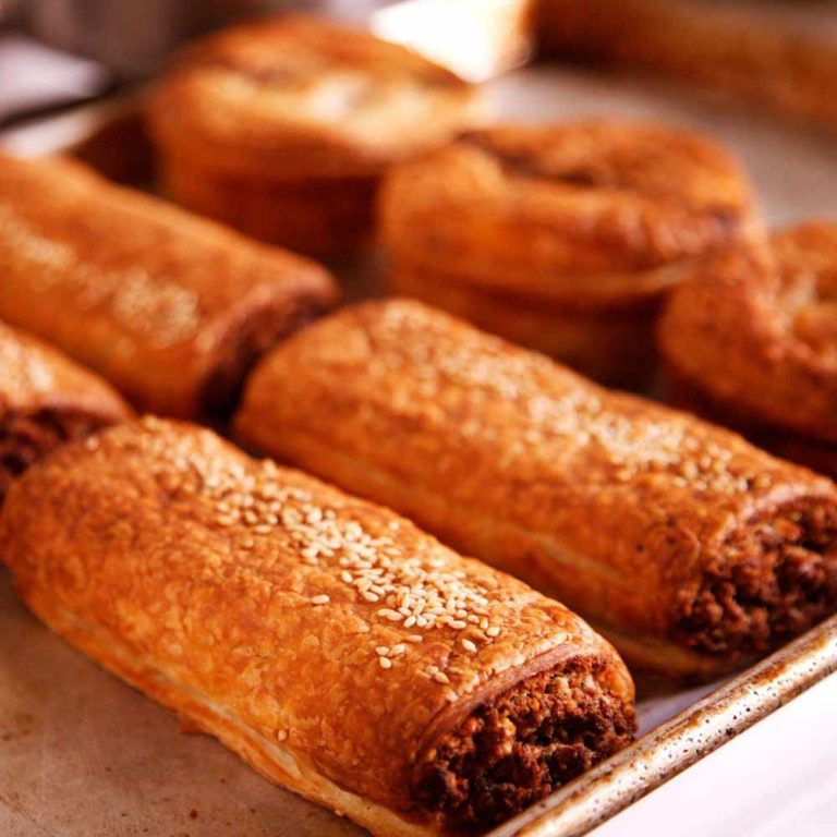 A baking tray with several baked vegan sausage rolls, some topped with sesame seeds, featuring golden, flaky pastry and visible plant-based filling—these are some of the best vegan pastries in Australia.