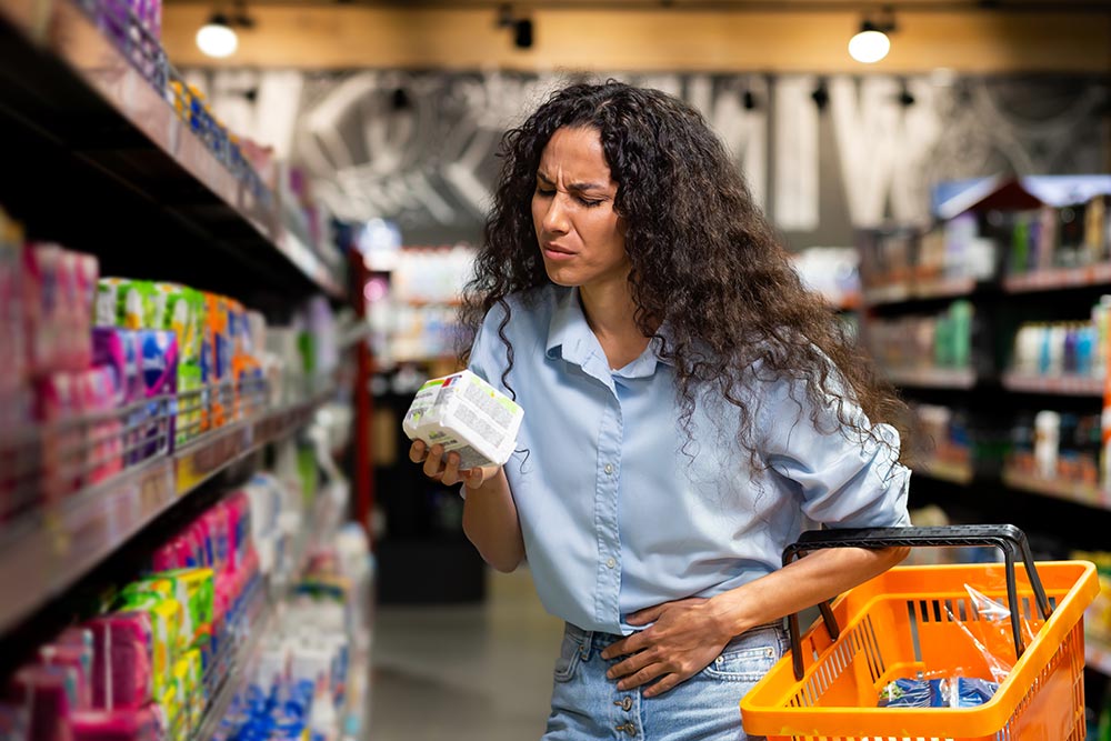 A woman with a shopping basket holds a product in her hand and squints to read the information on the packaging.