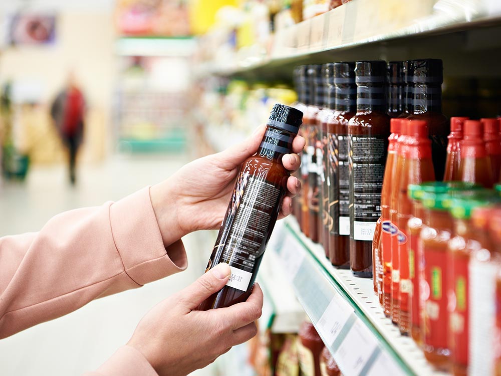 Hands are holding a bottle of what looks like a Mexican-style hot sauce in the supermarket.