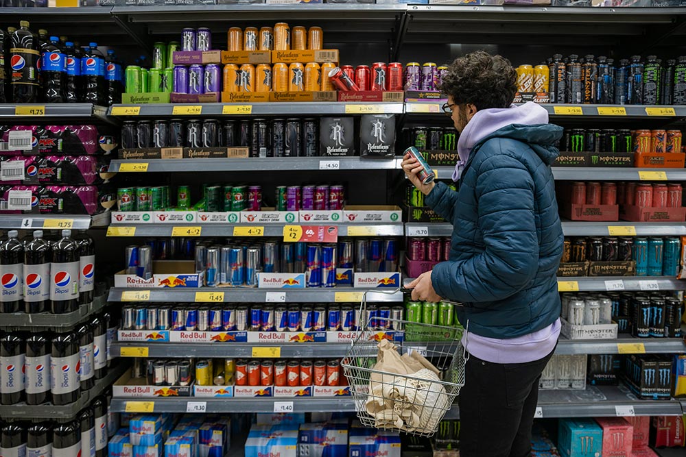 A man inspects a can of energy drinks in the soft drink aisle of the supermarket.