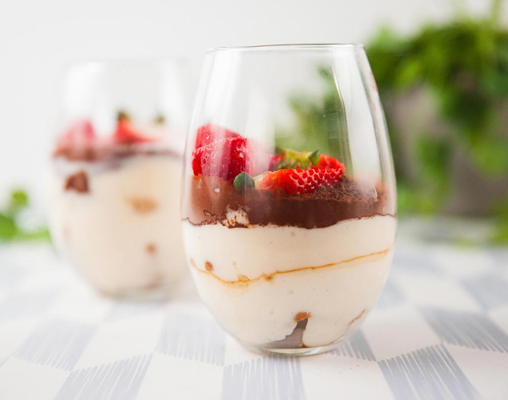 A frontal view of two clear glasses of tiramisu, topped with strawberries. 