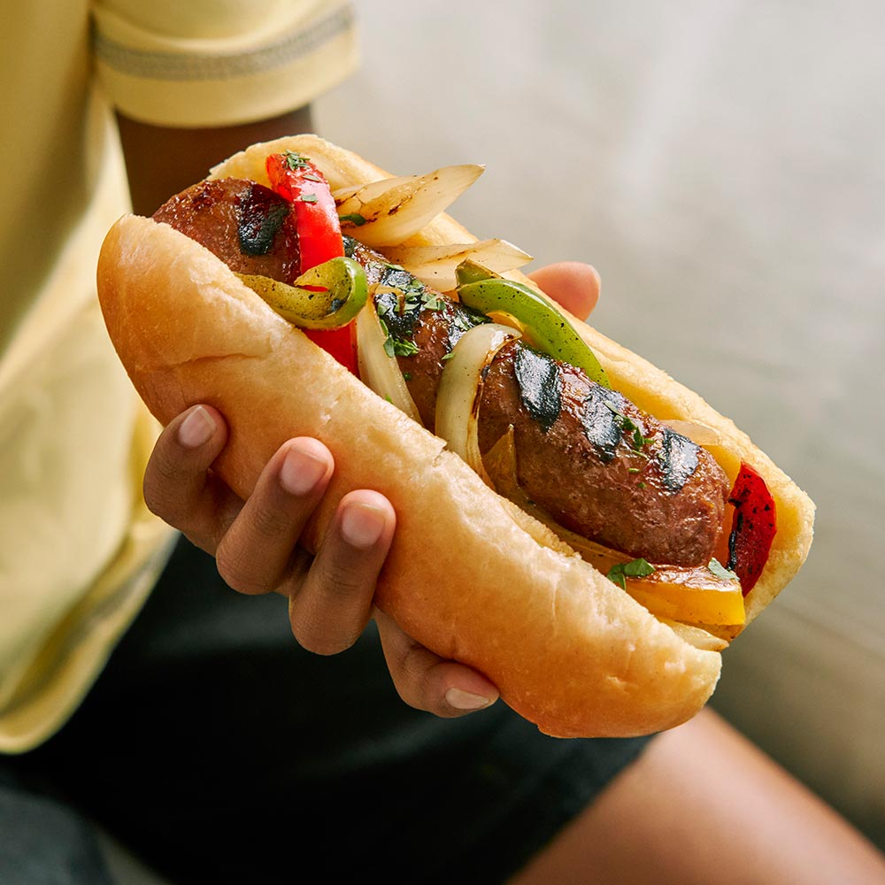 A person is sitting down holding a plant-based hot dog in their hand. 