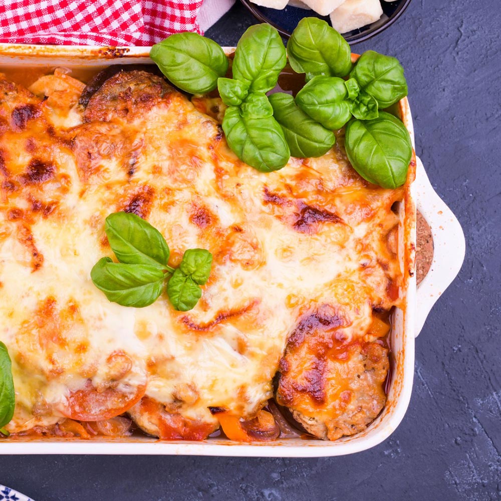 Overhead view of a tray of lasagne topped with creamy, gooey, melty cheese. Basil leaves are spread on top to garnish.