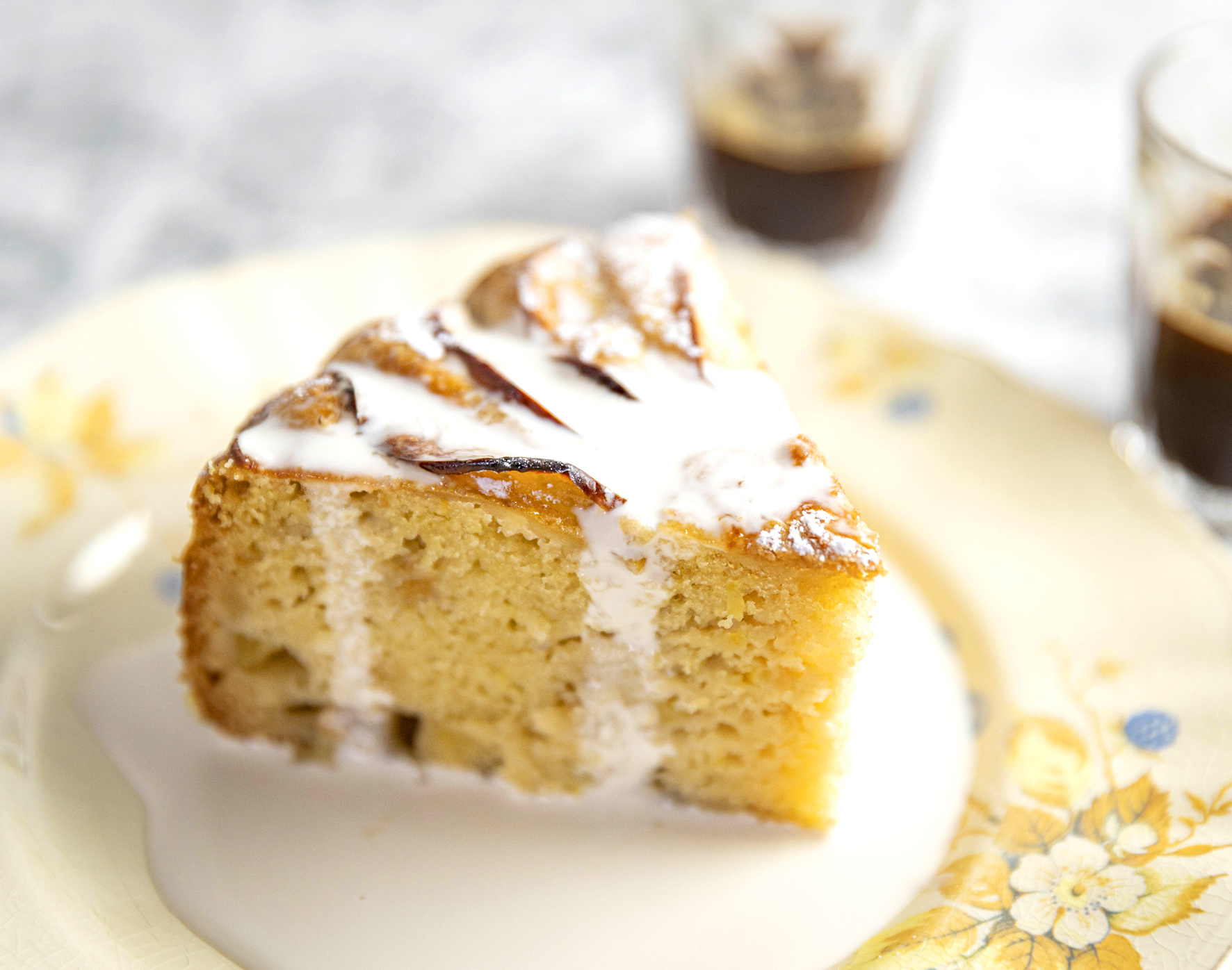 A single slice of lemon cake topped with cream. A pool of cream sits around the slice on the saucer beneath.