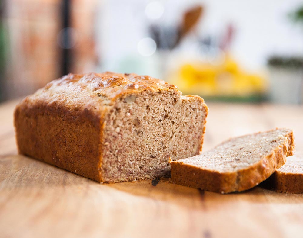 A loaf of banana bread sits on a shopping board, with several slices already cut. 