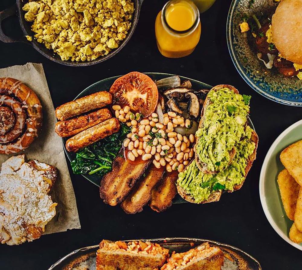 Overhead view of a an assortment of vegan foods available at the music festival. A full English breakfsat, toasties, burgers, pastries, and juice.