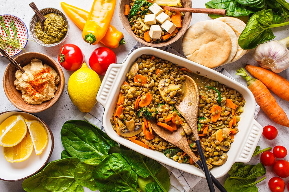 A healthy tray of lentil curry sits on a bench surrounded by fresh vegetables.