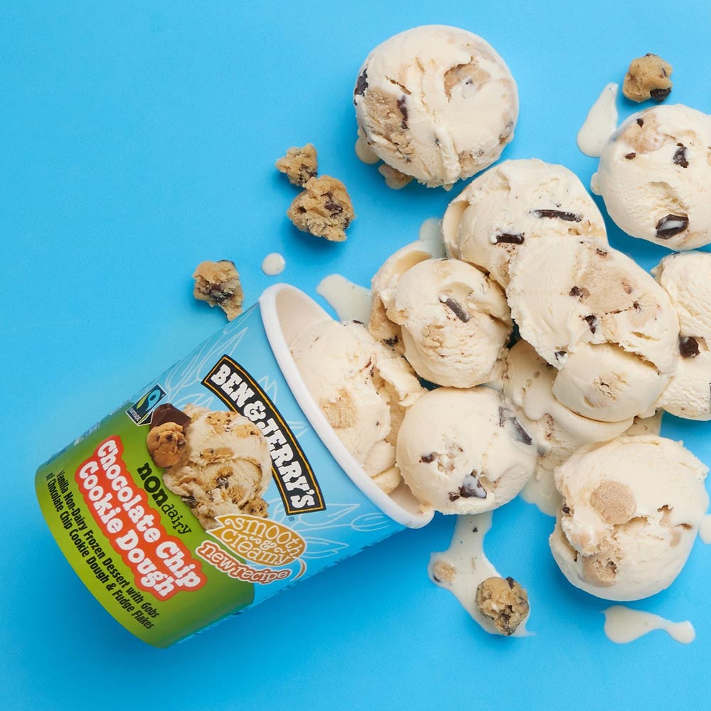 A tub of Ben & Jerry's dairy-free Choc Chip Cookie Dough ice cream on it's side, with scoops spilling out.