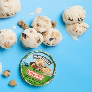 An overhead view of scoops of Ben & Jerry's dairy-free cookie dough ice cream on a blue background, with the lid showing.