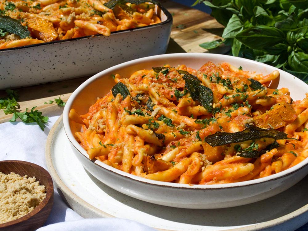 A creamy pumpkin fusili dish topped with sage sits in a bowl.