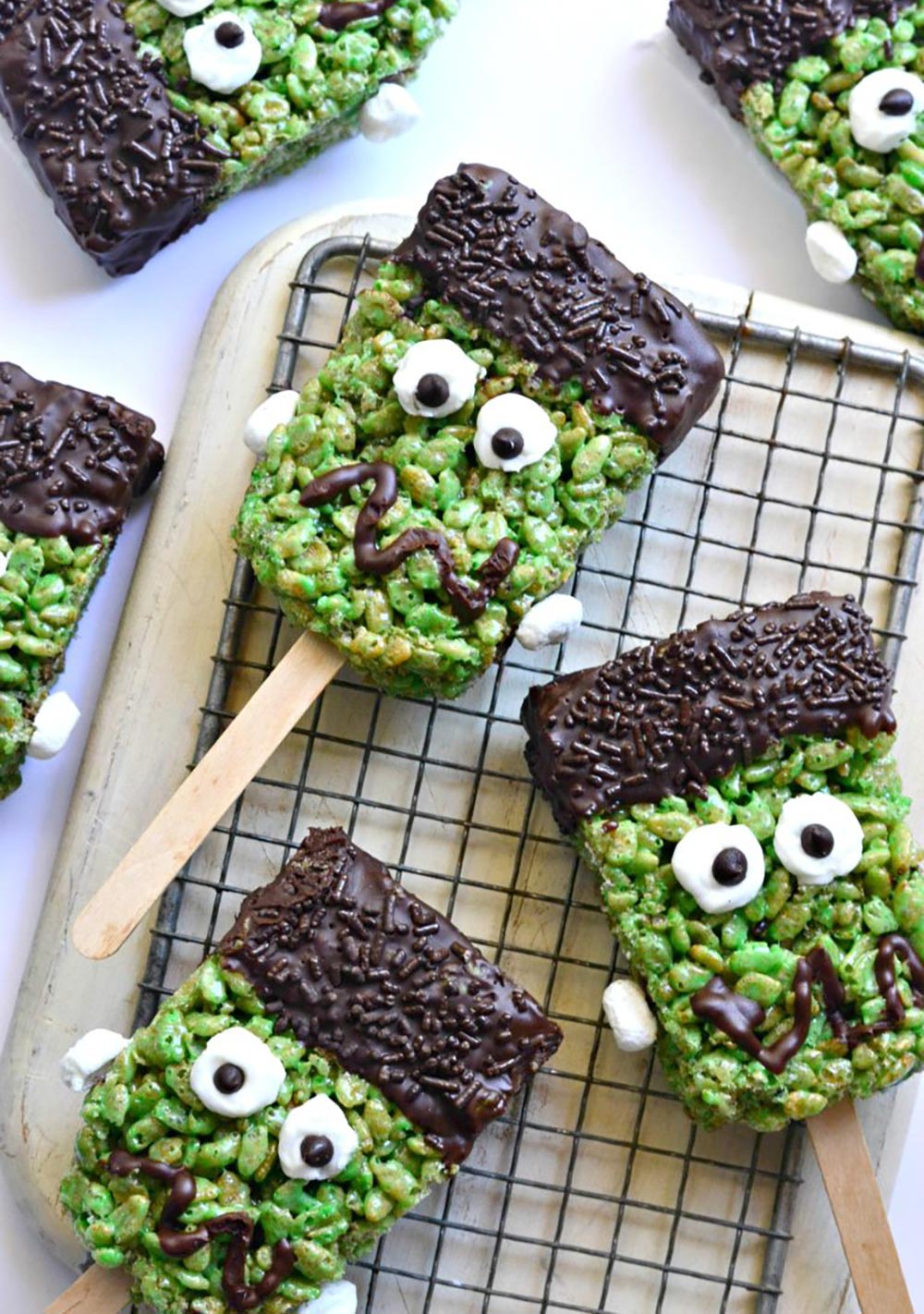 Green rice krispie treats on sticks have been decorated to look like Frankenstein's monster.