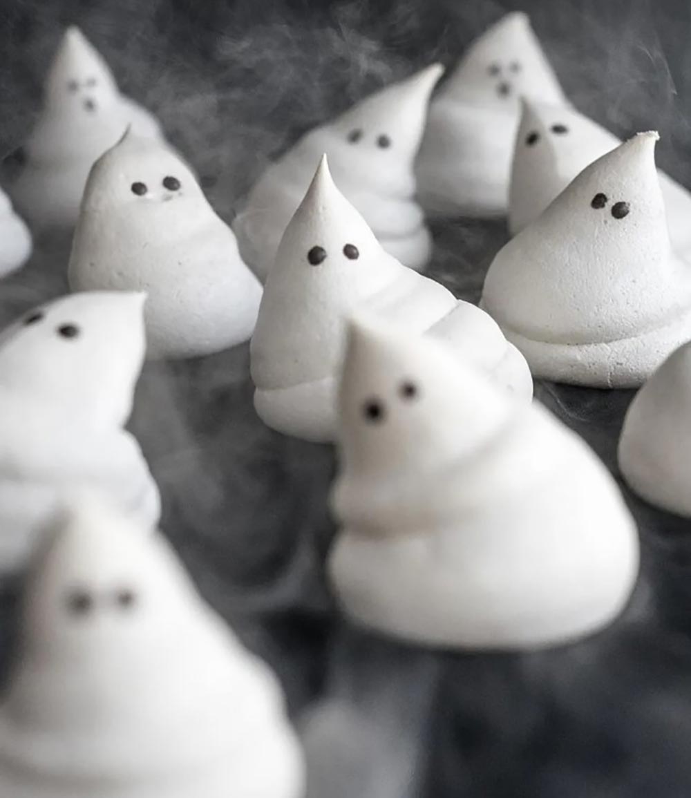 White meringue is piped into the shape of ghosts with little chocolate dots for eyes. 