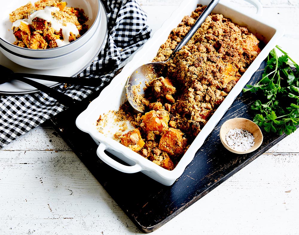 A savoury crumble in an oven dish sits on a table, with a serving in a nearby bowl.