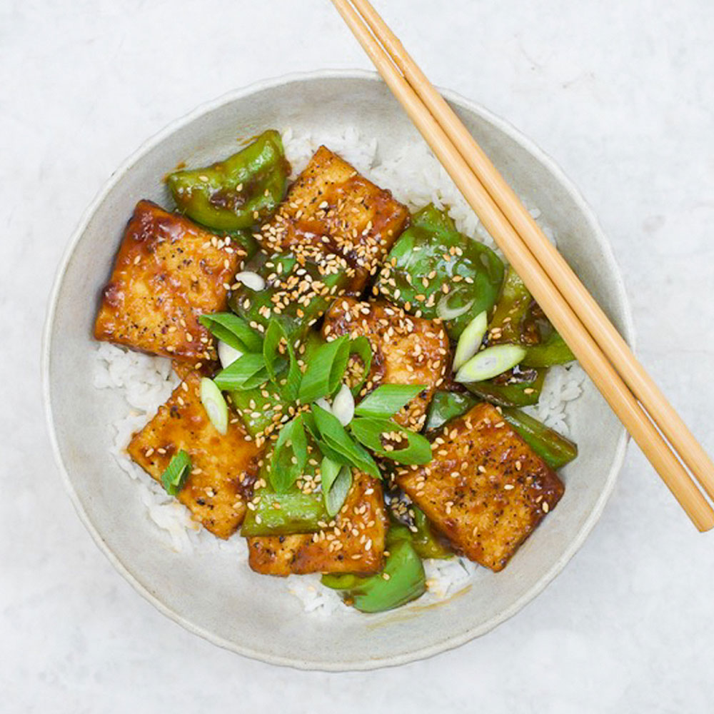 Overhead view of a peppery tofu and green capsicum stir-fry served on a bed of rice.