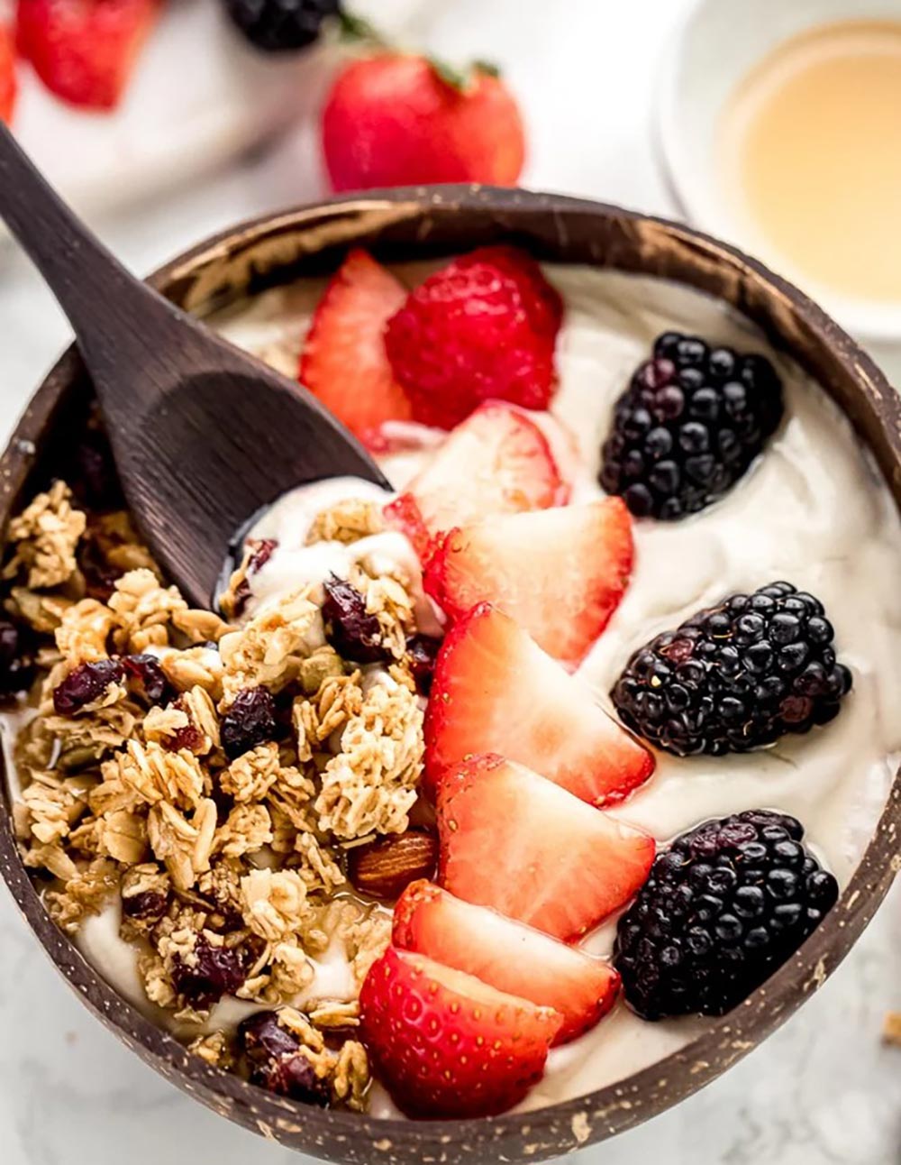 A coconut bowl filled with cashew yoghurt topped with oats, strawberries and blackberries.