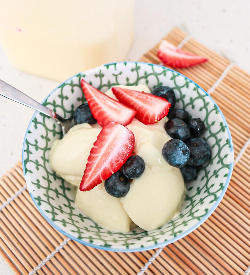 Overhead view of a patterned bowl filled with homemade Greek yoghurt topped with strawberries and blueberries.