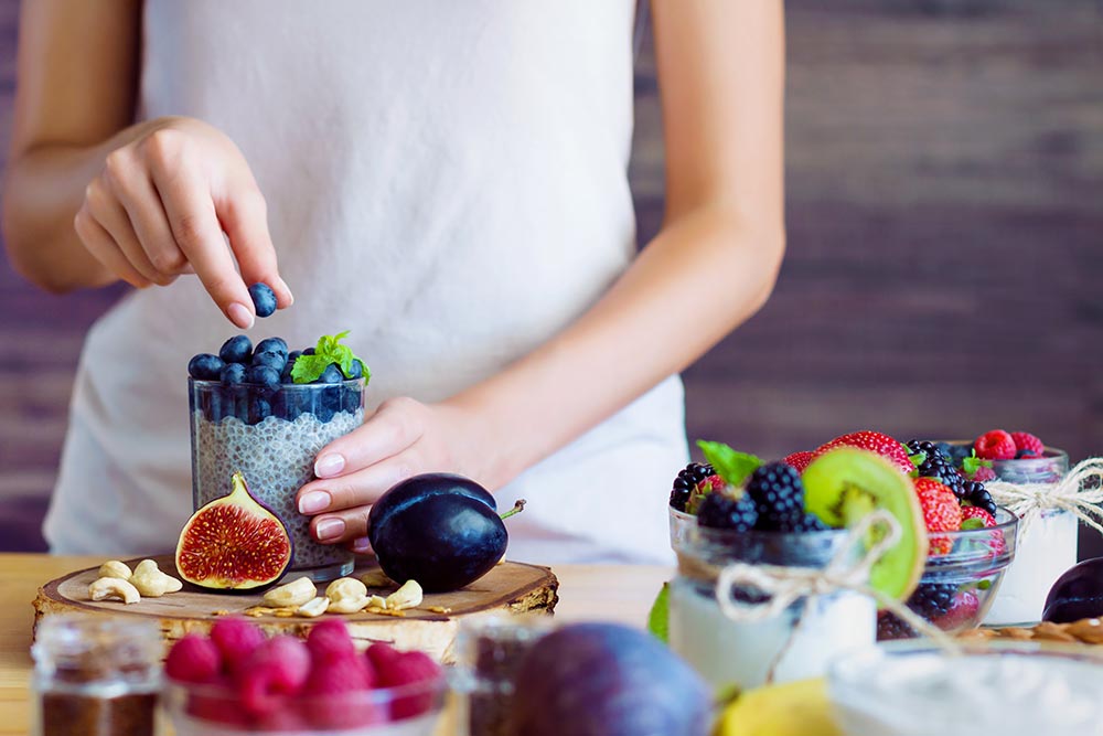 Female hands are preparing dairy-free yoghurt with chia and blueberries. 