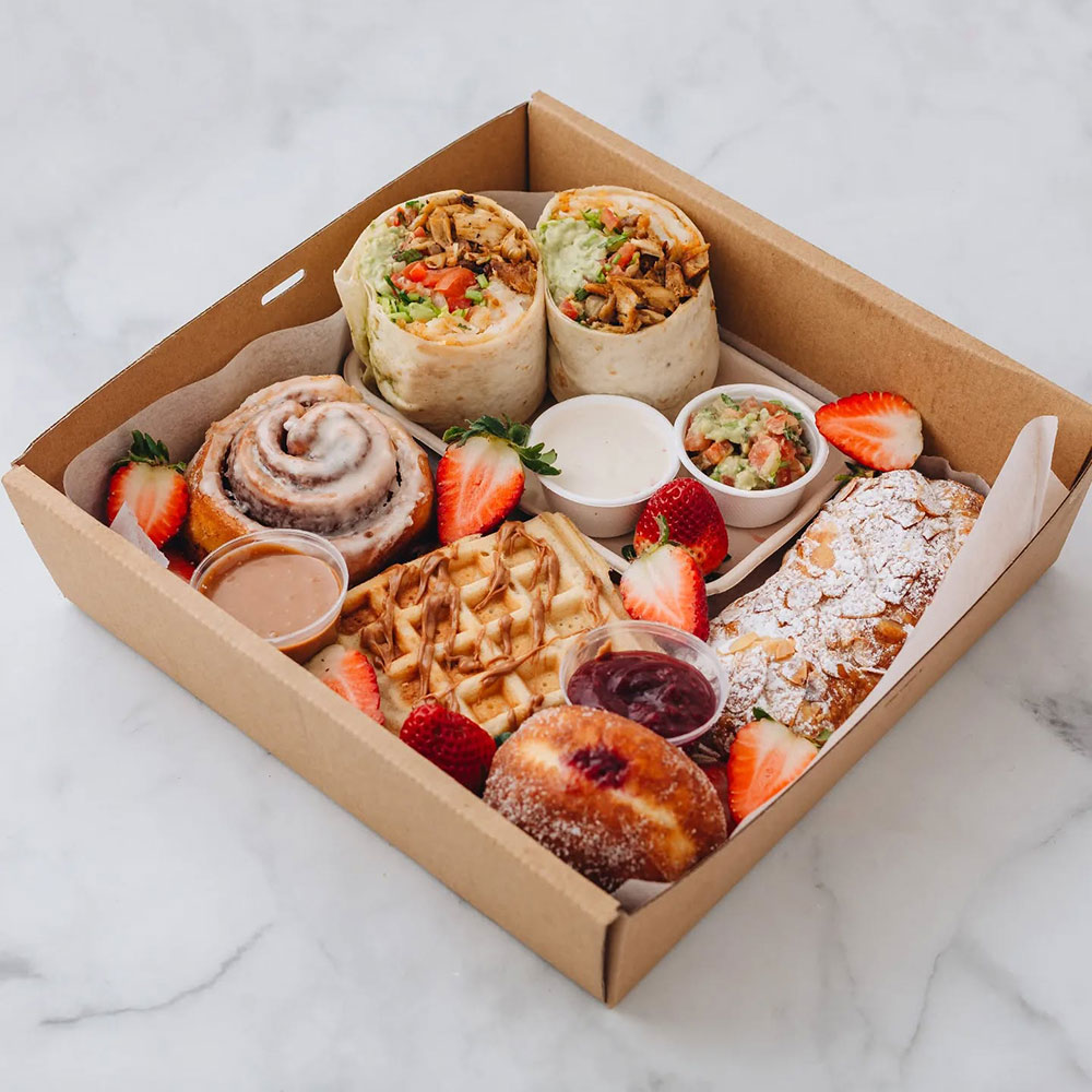 A grazing box displayed beautifully with a burrito, sweet scrolls and pastries, and strawberries.