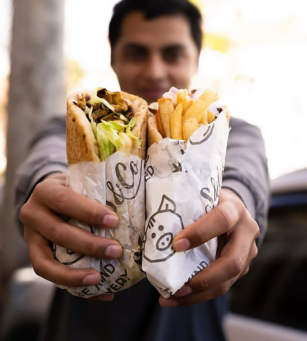 A man holds two vegan Yiros to camera.