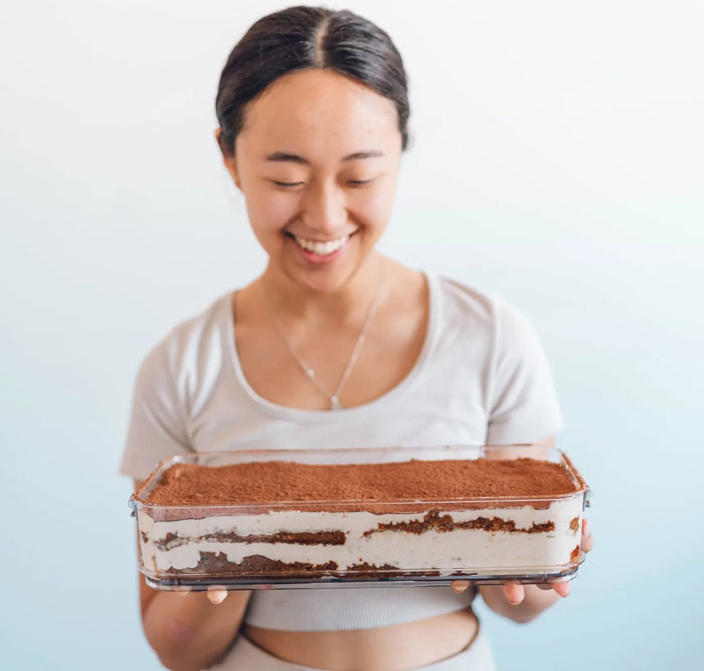 A woman holds a giant tiramisu tray in a glass dish, showing each delicious layer. 