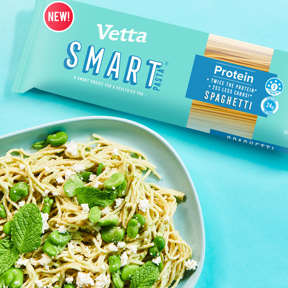 A pasta dish with vegan fetta and edamame on a serving plate with a packet of Vetta Smart Protein Pasta on a light blue background. 