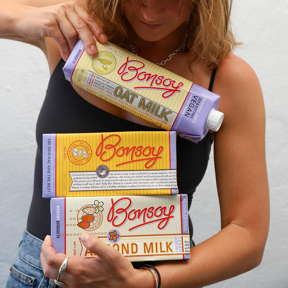 A person holds three different varieties of Bonsoy plant milk in their arms.