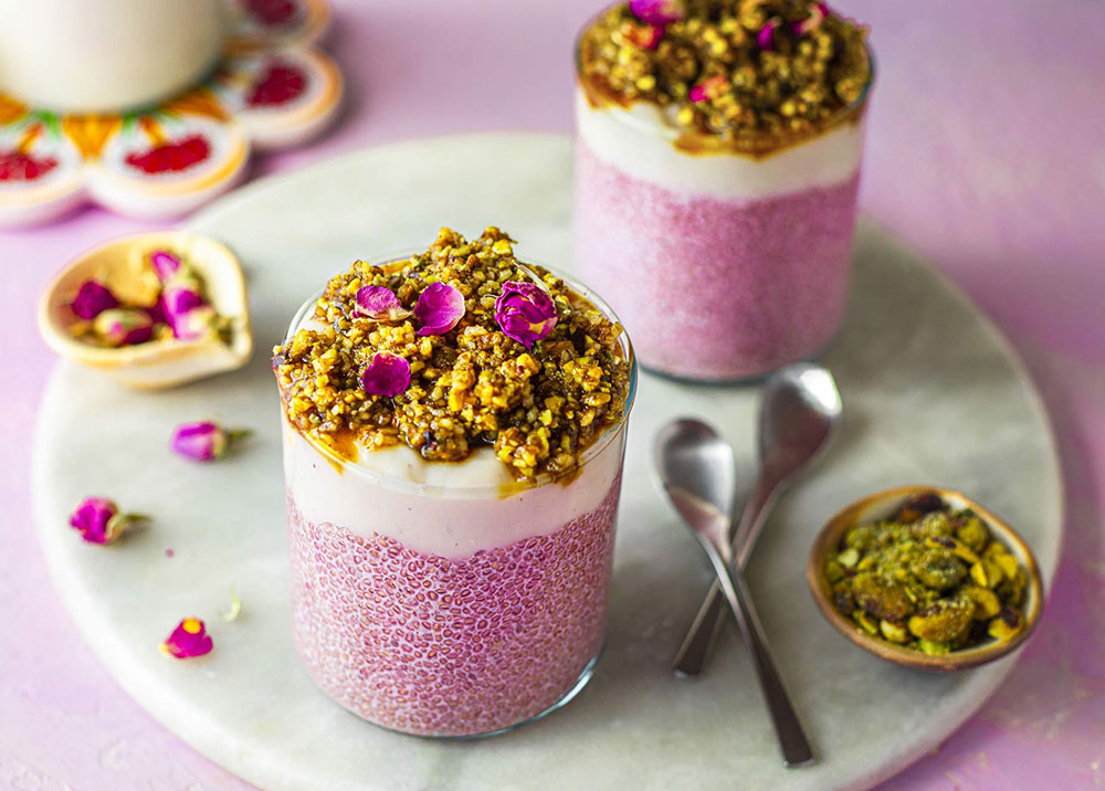 Two glasses filled with rosewater chia pudding topped with nuts are served on a plate. 