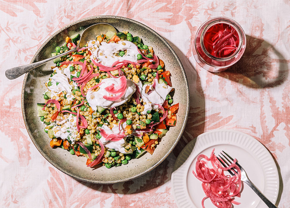 An overhead image of a farro and pickled onion salad on a pink patterned tablecloth.