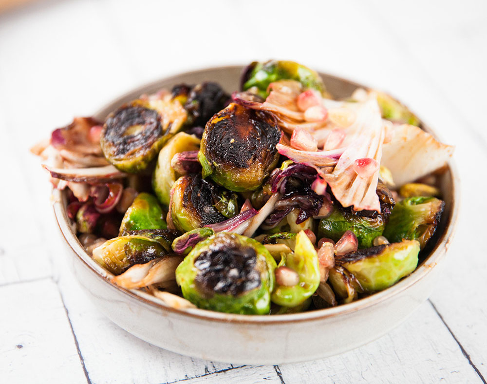 A bowl of charred Brussels sprouts on a white table.