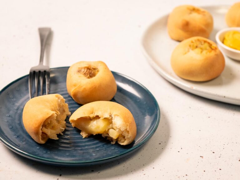 Potato Knishes sit on a plate, broken open to reveal a creamy filling.