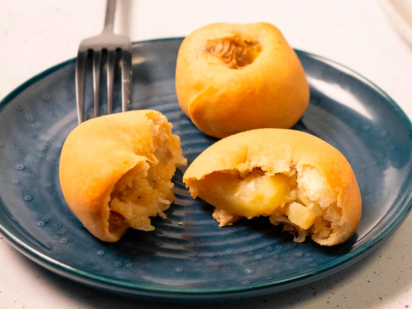 Potato Knishes sit on a plate, broken open to reveal a creamy filling.