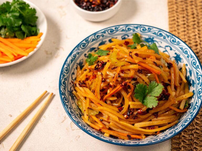 A crispy fried potato stir-fry is served in a blue patterned bowl with chopsticks to the side.