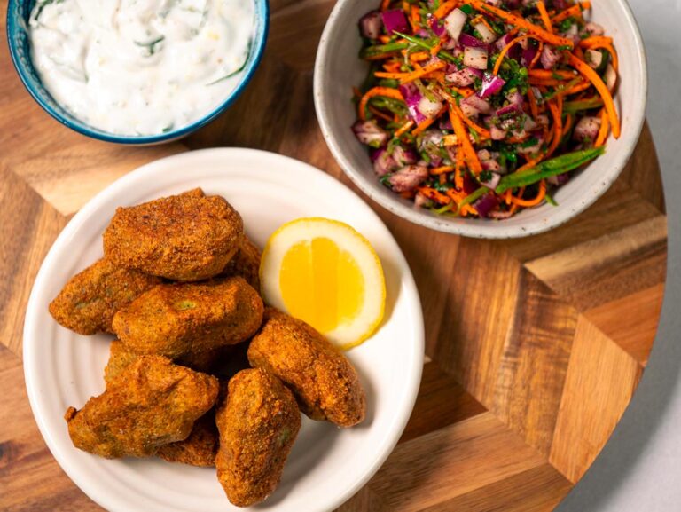 An overhead view of crispy golden tofu kofta in a bowl. A dish full of minted yoghurt for dipping, as well as a salad, sit nearby.