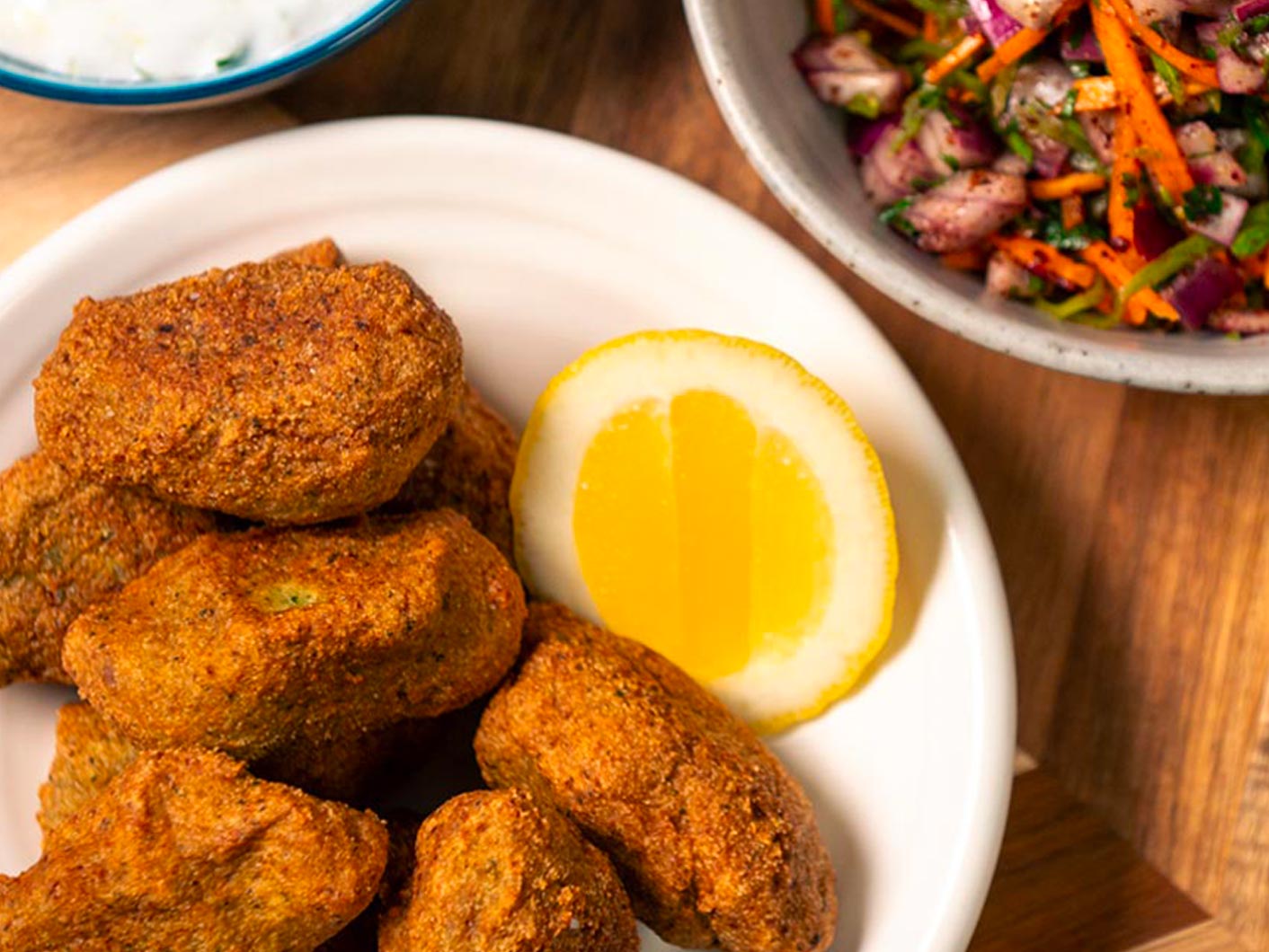 A close-up shot of crispy golden tofu kofta in a bowl, served with a wedge of lemon.