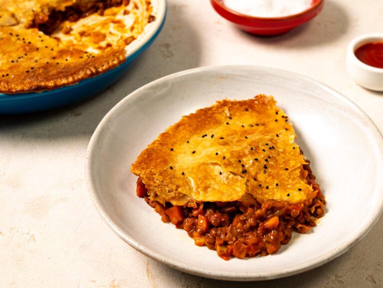 A white plate with a large slice of French lentil pot pie on it: hearty-looking veggie and lentil filling with a layer of pastry on top