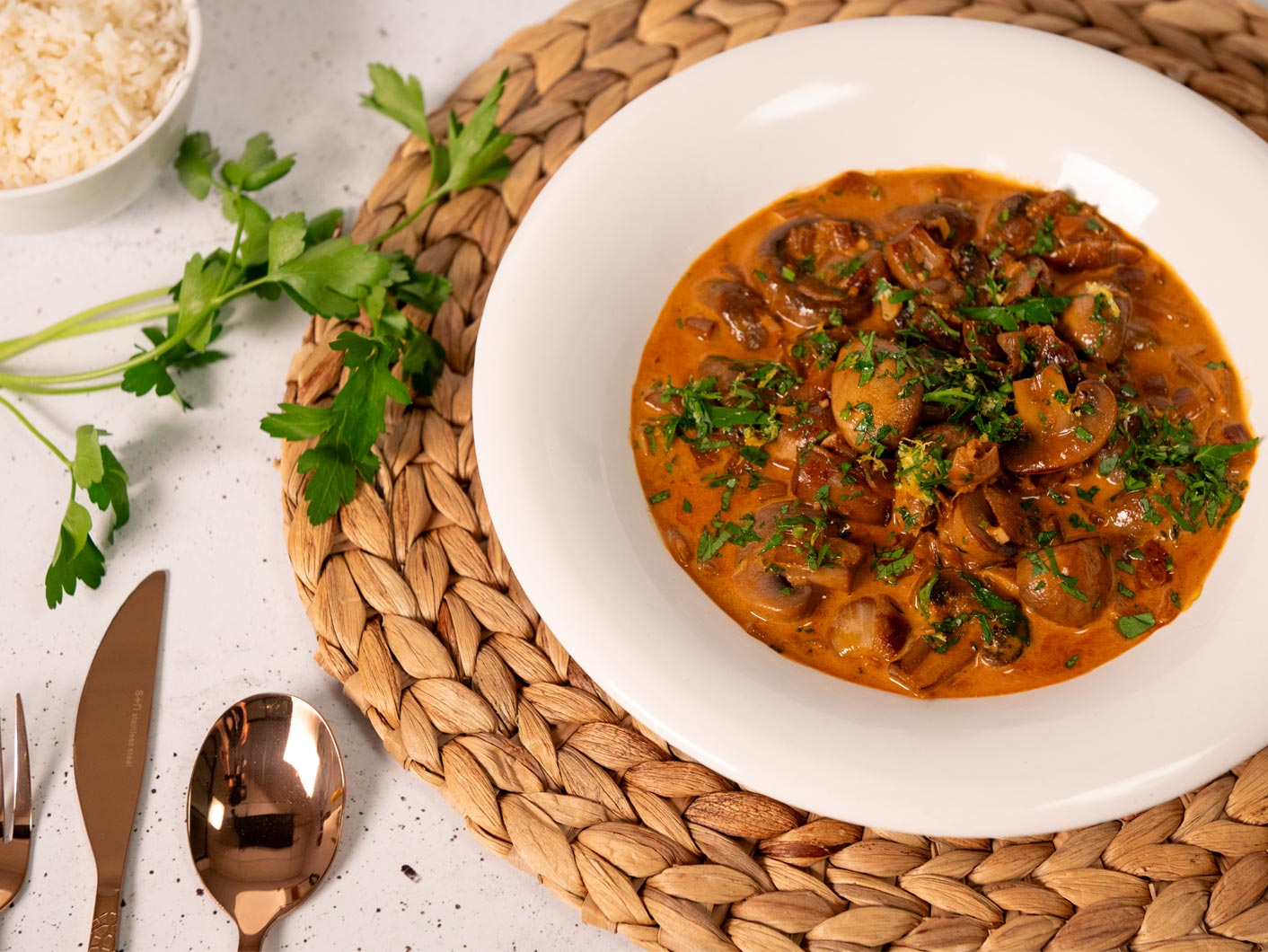 A large bowl of rich looking mushroom stroganoff -- thick, creamy, brown sauce loaded with mushrooms and finished with chopped parsley.