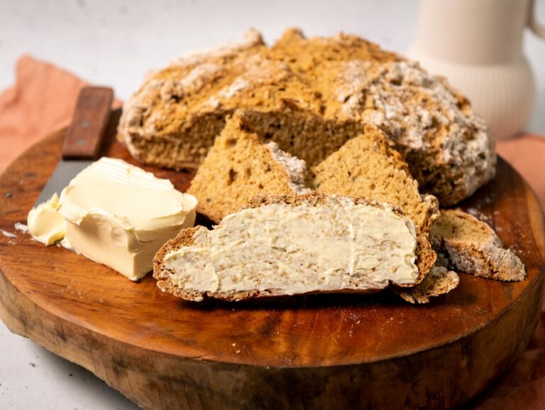 A golden loaf of Irish Soda Bread, alongside a few slices slathered with vegan butter.