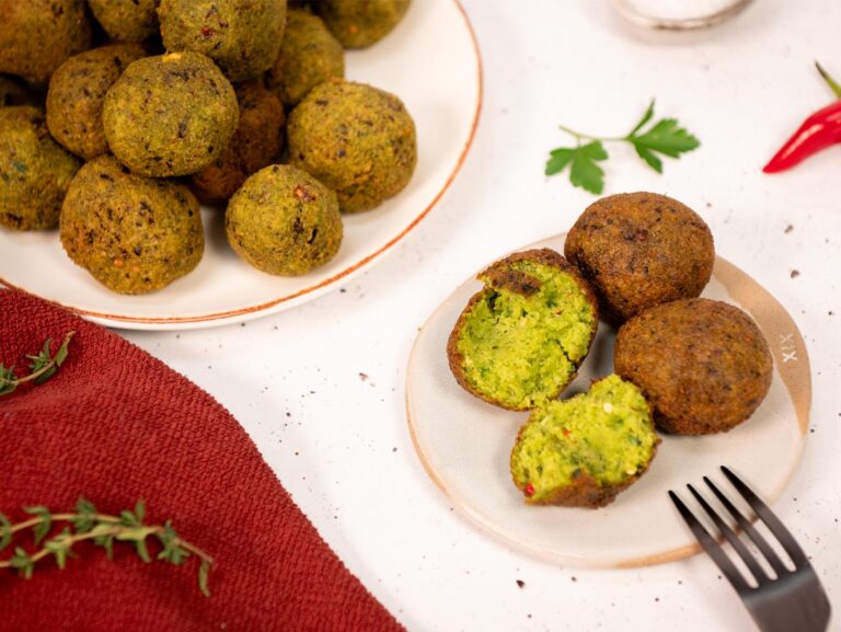 A plate full of gateaux piment (chilli cakes), or small golden-brown fried balls, alongside a smaller plate holding three of them. One is cracked open to reveal a lime green, doughy, crumbly centre.