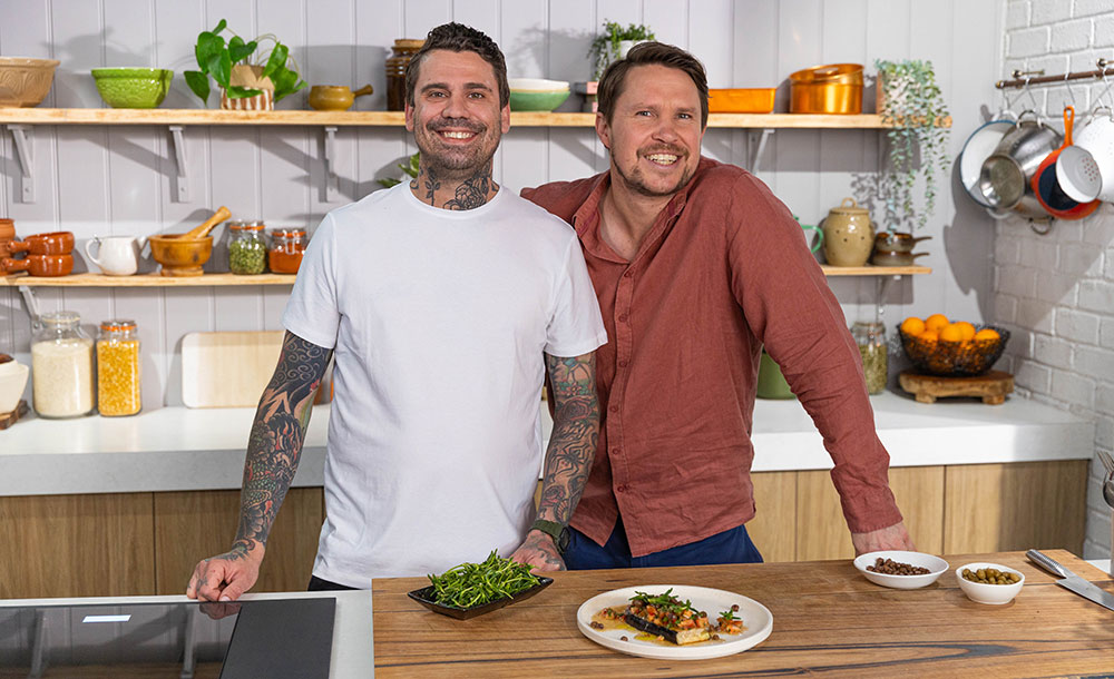 Simon Toohey and Jack Brown stand behind the Freshly Picked kitchen bench, smiling for a photo.