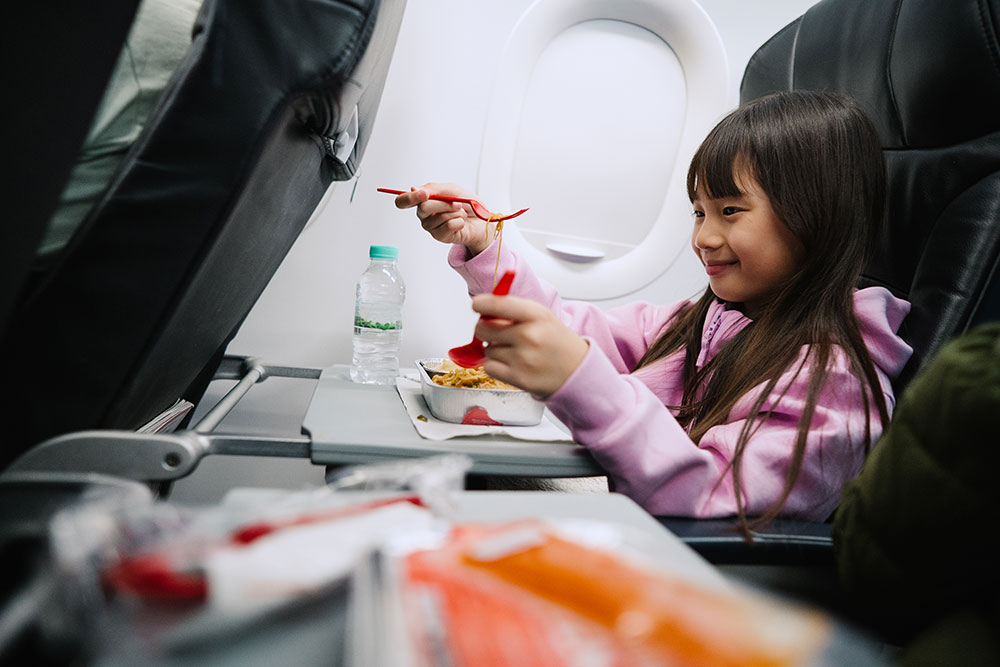 A young girl smiling as she's about to eat her airplane meal. 